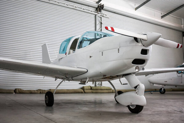 Small sports airplane with opened cockpit canopy in the hangar