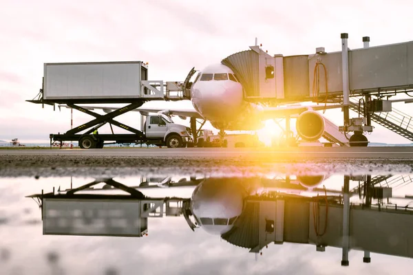 Ground handling of a white passenger airplane near the boarding bridge in the morning sun. Loading on-board catering from a truck to an aircraft