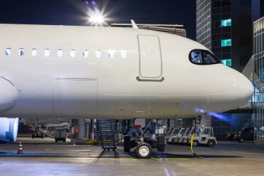 Gece hava köprüsü ve terminal yakınında havaalanı apronda beyaz yolcu jet uçağının ön kısmı