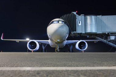 Hava köprüsü yakınında bir havaalanı gece önlük bir dış güç kaynağına bağlı beyaz bir yolcu uçağının ön görünümü