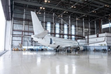 Beyaz yolcu uçağı hangarda. Uçak bakım altında. Uçuş işlemleri için mekanik sistemler denetleniyor