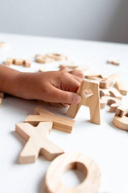 Beyaz yüzeyde tahta alfabe harfleriyle oynayan çocuk eli. Yüksek kalite.