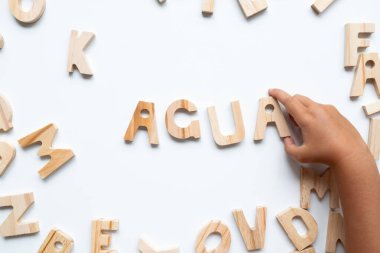 Child hand arranging wooden letters on white background. High quality.