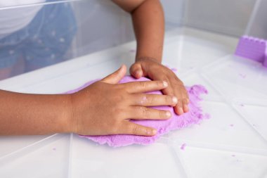 Beyaz masada mor kinetik kumla oynayan bir çocuk. Yüksek kalite.