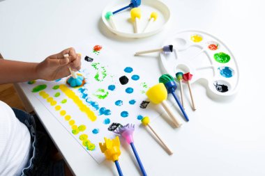 Child engaged in creative painting with foam brushes, caucasian, young. High quality.