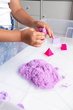 Child playing with purple kinetic sand and geometric molds. High quality.