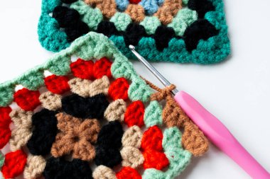 Colorful crochet granny squares with pink hook on white background. High quality.