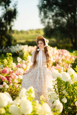 Klasik şık elbiseli güzel bir kadın parkta ortancalar arasında poz veriyor.