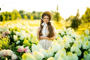 Klasik şık elbiseli güzel bir kadın parkta ortancalar arasında poz veriyor.