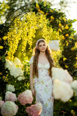 Klasik şık elbiseli güzel bir kadın parkta ortancalar arasında poz veriyor.