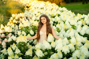 Klasik şık elbiseli güzel bir kadın parkta ortancalar arasında poz veriyor.