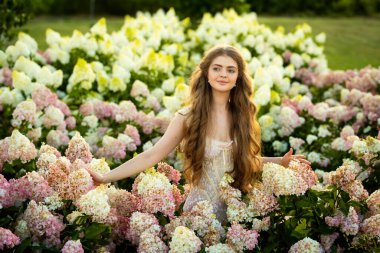 Klasik şık elbiseli güzel bir kadın parkta ortancalar arasında poz veriyor.