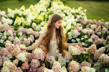 Klasik şık elbiseli güzel bir kadın parkta ortancalar arasında poz veriyor.