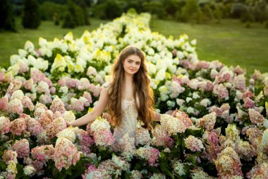 Klasik şık elbiseli güzel bir kadın parkta ortancalar arasında poz veriyor.