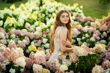 Klasik şık elbiseli güzel bir kadın parkta ortancalar arasında poz veriyor.