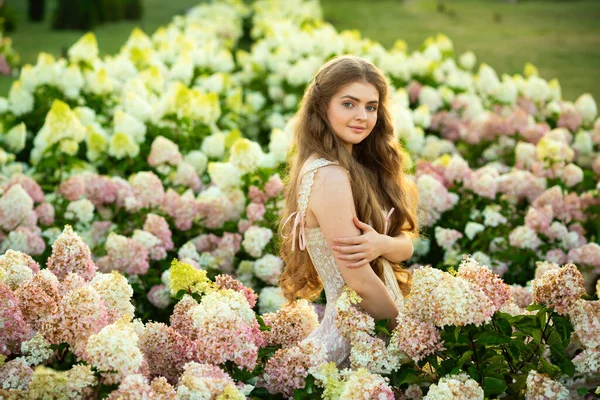 Klasik şık elbiseli güzel bir kadın parkta ortancalar arasında poz veriyor.