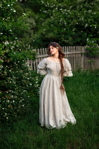 Красивая женщина с длинной косой в винтажном платье позирует в жасминовые цветы в сельской местности