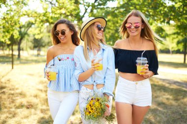 Üç güzel kız parkta sarı suyu içme ve eğlenmek. Mükemmel güneşli havalarda. Güzel resimler. Süper ruh hali. Yaz konsepti.