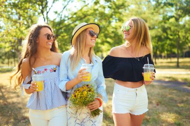 Üç güzel kız parkta sarı suyu içme ve eğlenmek. Mükemmel güneşli havalarda. Güzel resimler. Süper ruh hali. Yaz konsepti.