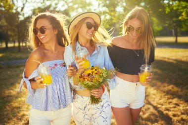 Üç güzel kız parkta sarı suyu içme ve eğlenmek. Mükemmel güneşli havalarda. Güzel resimler. Süper ruh hali. Yaz konsepti.