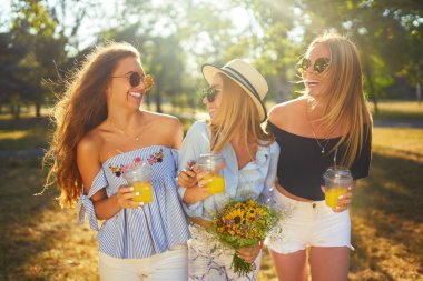 Üç güzel kız parkta sarı suyu içme ve eğlenmek. Mükemmel güneşli havalarda. Güzel resimler. Süper ruh hali. Yaz konsepti.