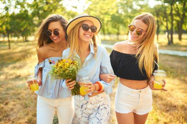 Üç güzel kız parkta sarı suyu içme ve eğlenmek. Mükemmel güneşli havalarda. Güzel resimler. Süper ruh hali. Yaz konsepti.