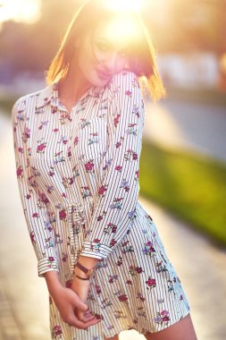 Güzel genç bir bayanla uzun sağlıklı saç ve şirin elbise sokakta yürümek. Sıcak yaz gecesi. Gün batımı. Yaşam tarzı kavramı. 