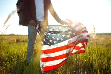 4 Temmuz. Amerikan Flag.Patriotic tatil. Amerika bayrağı ile seyahat. Adam bir şapka, bir sırt çantası, bir tişört ve kot pantolon giyiyor. Güzel gün batımı ışık. Amerikan tarzı. 