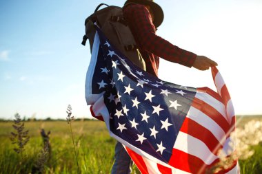 4 Temmuz. Amerikan Flag.Patriotic tatil. Amerika bayrağı ile seyahat. Adam bir şapka, bir sırt çantası, bir tişört ve kot pantolon giyiyor. Güzel gün batımı ışık. Amerikan tarzı. 