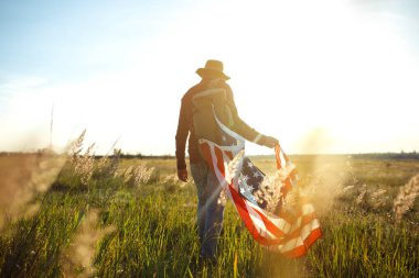 4 Temmuz. Amerikan Flag.Patriotic tatil. Amerika bayrağı ile seyahat. Adam bir şapka, bir sırt çantası, bir tişört ve kot pantolon giyiyor. Güzel gün batımı ışık. Amerikan tarzı. 