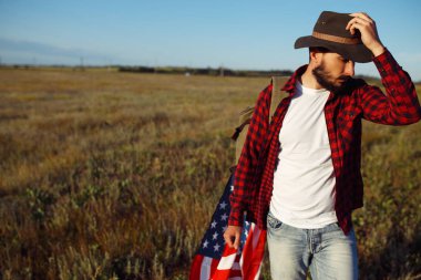 4 Temmuz. Amerikan Flag.Patriotic tatil. Amerika bayrağı ile seyahat. Adam bir şapka, bir sırt çantası, bir tişört ve kot pantolon giyiyor. Güzel gün batımı ışık. Amerikan tarzı. 