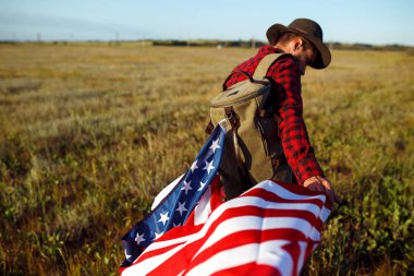 4 Temmuz. Amerikan Flag.Patriotic tatil. Amerika bayrağı ile seyahat. Adam bir şapka, bir sırt çantası, bir tişört ve kot pantolon giyiyor. Güzel gün batımı ışık. Amerikan tarzı. 