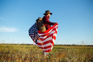 4 Temmuz. Amerikan Flag.Patriotic tatil. Amerika bayrağı ile seyahat. Adam bir şapka, bir sırt çantası, bir tişört ve kot pantolon giyiyor. Güzel gün batımı ışık. Amerikan tarzı. 