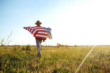 4 Temmuz. Amerikan Flag.Patriotic tatil. Amerika bayrağı ile seyahat. Adam bir şapka, bir sırt çantası, bir tişört ve kot pantolon giyiyor. Güzel gün batımı ışık. Amerikan tarzı. 
