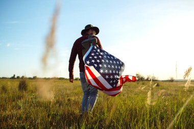 4 Temmuz. Amerikan Flag.Patriotic tatil. Amerika bayrağı ile seyahat. Adam bir şapka, bir sırt çantası, bir tişört ve kot pantolon giyiyor. Güzel gün batımı ışık. Amerikan tarzı. 