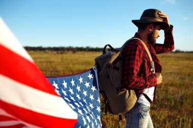 4 Temmuz. Amerikan Flag.Patriotic tatil. Amerika bayrağı ile seyahat. Adam bir şapka, bir sırt çantası, bir tişört ve kot pantolon giyiyor. Güzel gün batımı ışık. Amerikan tarzı. 