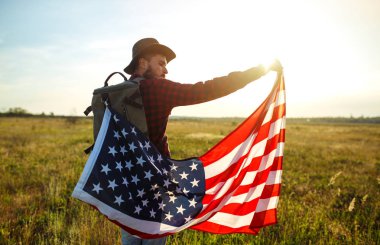 4 Temmuz. Amerikan Flag.Patriotic tatil. Amerika bayrağı ile seyahat. Adam bir şapka, bir sırt çantası, bir tişört ve kot pantolon giyiyor. Güzel gün batımı ışık. Amerikan tarzı. 