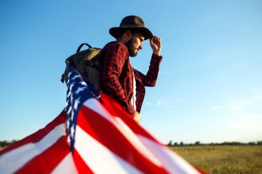 4 Temmuz. Amerikan Flag.Patriotic tatil. Amerika bayrağı ile seyahat. Adam bir şapka, bir sırt çantası, bir tişört ve kot pantolon giyiyor. Güzel gün batımı ışık. Amerikan tarzı. 