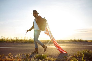 4 Temmuz. Amerikan Flag.Patriotic tatil. Amerika bayrağı ile seyahat. Adam bir şapka, bir sırt çantası, bir tişört ve kot pantolon giyiyor. Güzel gün batımı ışık. Amerikan tarzı. 