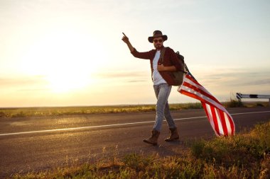 4 Temmuz. Amerikan Flag.Patriotic tatil. Amerika bayrağı ile seyahat. Adam bir şapka, bir sırt çantası, bir tişört ve kot pantolon giyiyor. Güzel gün batımı ışık. Amerikan tarzı. 