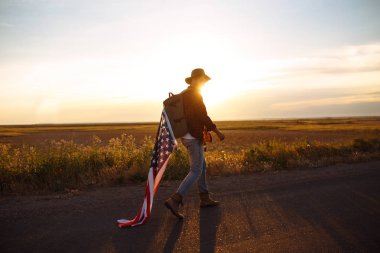 4 Temmuz. Amerikan Flag.Patriotic tatil. Amerika bayrağı ile seyahat. Adam bir şapka, bir sırt çantası, bir tişört ve kot pantolon giyiyor. Güzel gün batımı ışık. Amerikan tarzı. 