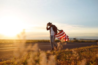 4 Temmuz. Amerikan Flag.Patriotic tatil. Amerika bayrağı ile seyahat. Adam bir şapka, bir sırt çantası, bir tişört ve kot pantolon giyiyor. Güzel gün batımı ışık. Amerikan tarzı. 