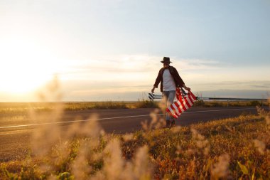 4 Temmuz. Amerikan Flag.Patriotic tatil. Amerika bayrağı ile seyahat. Adam bir şapka, bir sırt çantası, bir tişört ve kot pantolon giyiyor. Güzel gün batımı ışık. Amerikan tarzı. 