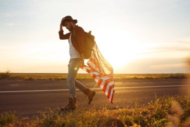 4 Temmuz. Amerikan Flag.Patriotic tatil. Amerika bayrağı ile seyahat. Adam bir şapka, bir sırt çantası, bir tişört ve kot pantolon giyiyor. Güzel gün batımı ışık. Amerikan tarzı. 