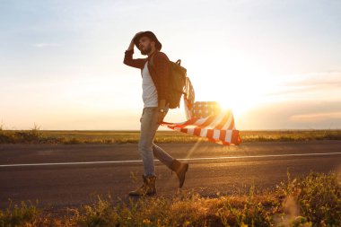 4 Temmuz. Amerikan Flag.Patriotic tatil. Amerika bayrağı ile seyahat. Adam bir şapka, bir sırt çantası, bir tişört ve kot pantolon giyiyor. Güzel gün batımı ışık. Amerikan tarzı. 