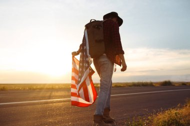 4 Temmuz. Amerikan Flag.Patriotic tatil. Amerika bayrağı ile seyahat. Adam bir şapka, bir sırt çantası, bir tişört ve kot pantolon giyiyor. Güzel gün batımı ışık. Amerikan tarzı. 