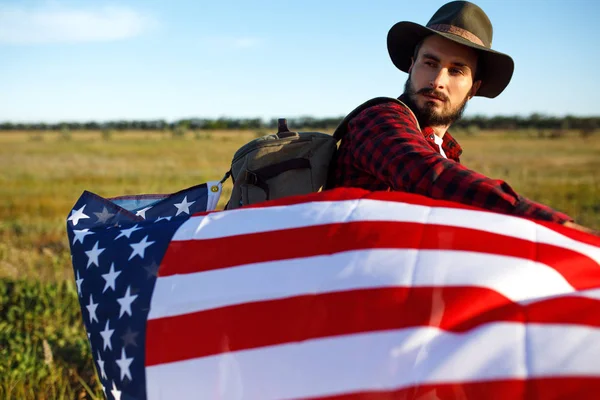 4 Temmuz. Amerikan Flag.Patriotic tatil. Amerika bayrağı ile seyahat. Adam bir şapka, bir sırt çantası, bir tişört ve kot pantolon giyiyor. Güzel gün batımı ışık. Amerikan tarzı. 