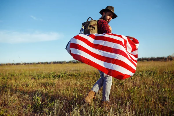 4 Temmuz. Amerikan Flag.Patriotic tatil. Amerika bayrağı ile seyahat. Adam bir şapka, bir sırt çantası, bir tişört ve kot pantolon giyiyor. Güzel gün batımı ışık. Amerikan tarzı. 