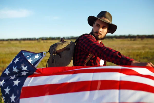 4 Temmuz. Amerikan Flag.Patriotic tatil. Amerika bayrağı ile seyahat. Adam bir şapka, bir sırt çantası, bir tişört ve kot pantolon giyiyor. Güzel gün batımı ışık. Amerikan tarzı. 