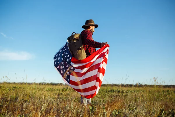 4 Temmuz. Amerikan Flag.Patriotic tatil. Amerika bayrağı ile seyahat. Adam bir şapka, bir sırt çantası, bir tişört ve kot pantolon giyiyor. Güzel gün batımı ışık. Amerikan tarzı. 